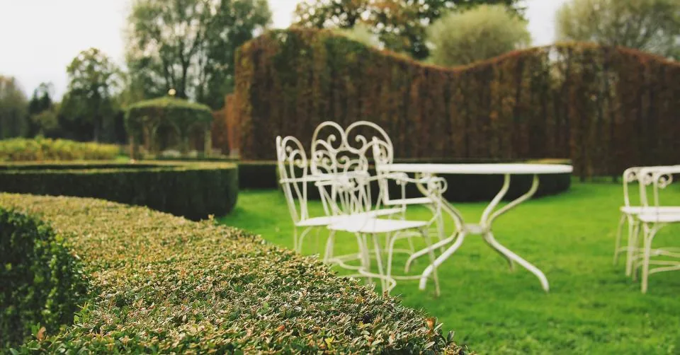 Neatly trimmed hedges and a lawn with white garden furniture