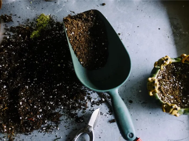 A trowel in fresh potting soil next to plant pots